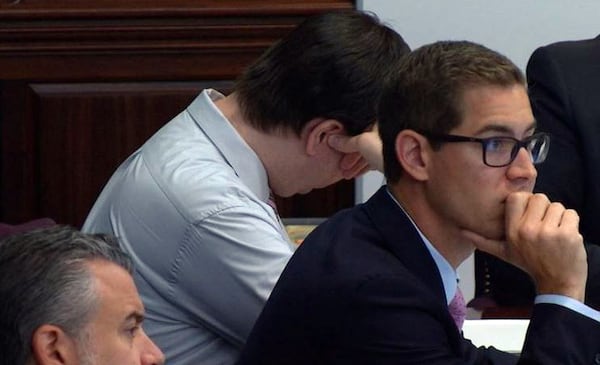 Defendant Ross Harris averts his eyes as the prosecution projected photos of his son’s body onto a large screen in the courtroom. On the right is defense attorney Carlos Rodriguez. Lead defense attorney Maddox Kilgore is at lower left. (Screen capture from WSB-TV video)