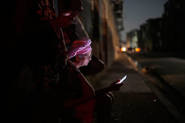 Residents look at their cell phones on the street during a general blackout in Havana, Cuba, Friday, March 14, 2025. (AP Photo/Ramon Espinosa)