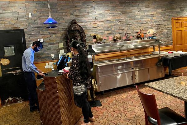 A customer picks up a takeout order at Cafe Bombay on Briarcliff Road, where the lunchtime steam tables sit empty, thanks to COVID-19 restrictions. Wendell Brock for The Atlanta Journal-Constitution