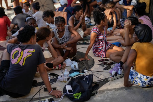 Residents charge their electronic devices on a street during a general blackout in Havana, Saturday, March 15, 2025. (AP Photo/Ramon Espinosa)