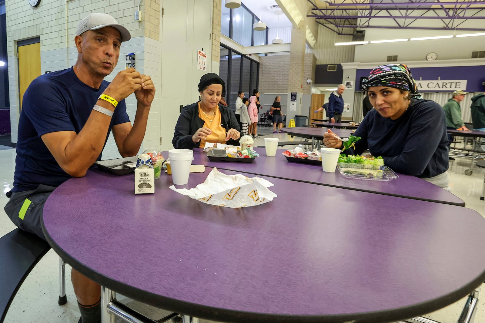 Muhamed Aftah, Fatimah Aftah and Senna Aftah eat a meal at a hurricane shelter at River Ridge Middle/High School in preparation for Hurricane Milton, Wednesday, Oct. 9, 2024, in New Port Richey, Fla. (AP Photo/Mike Carlson)