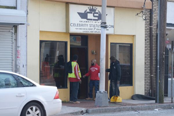 Shop owners clean up broken glass after Friday’s shooting. (Credit: David Barnes / For the AJC)