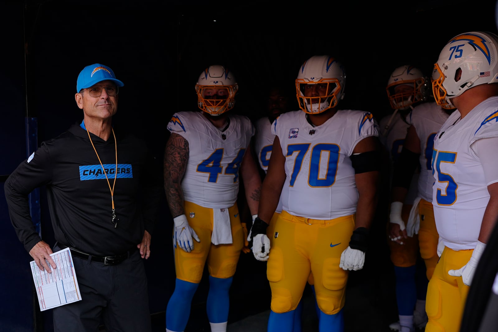 Los Angeles Chargers head coach Jim Harbaugh stands in a tunnel with players before an NFL football game against the Denver Broncos, Sunday, Oct. 13, 2024, in Denver. (AP Photo/David Zalubowski)