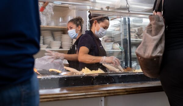 200717-Tucker-Ingred Cruez, left, and Marie Rodriguez help customers from behind acrylic panels during the lunch rush at Matthews Cafeteria on Main Street in Tucker on Friday afternoon July 17, 2020. The dining institution, established in 1955, ask customers to wear masks, added the acrylic dividers, made separate entrance and exit doors and have drive-up service.  Ben Gray for the Atlanta Journal-Constitution