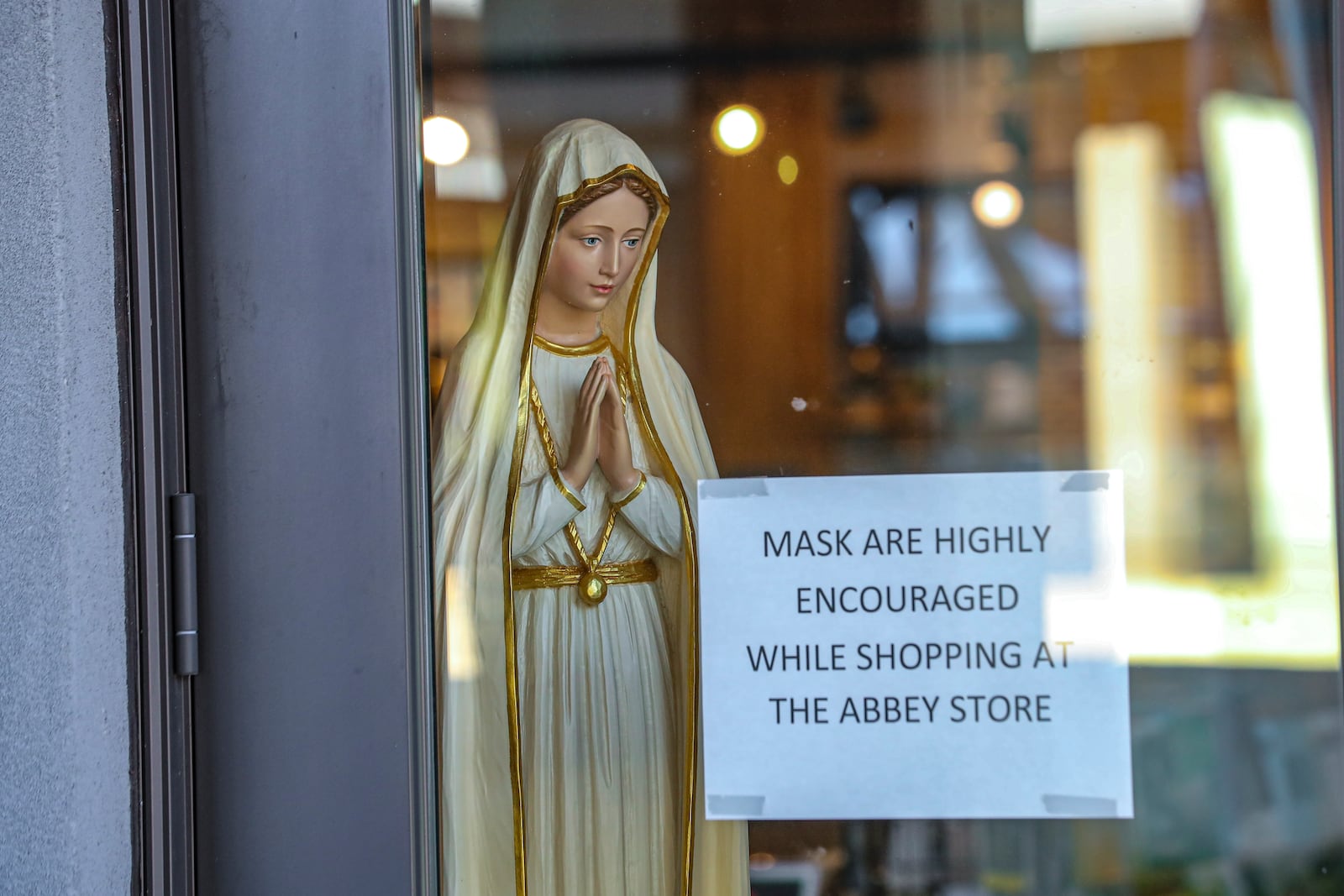 A statue of Our Lady of Fatima peers from inside the Abbey Gift Store where signs encourage visitors to wear masks on Thursday, Jan 13, 2022. The monks of The Holy Spirit Monastery in Conyers have been locked down during the pandemic as well as all of their business enterprises. Their gift store and Heritage Center reopened during the Christmas season and have remained open. (John Spink / John.Spink@ajc.com)

