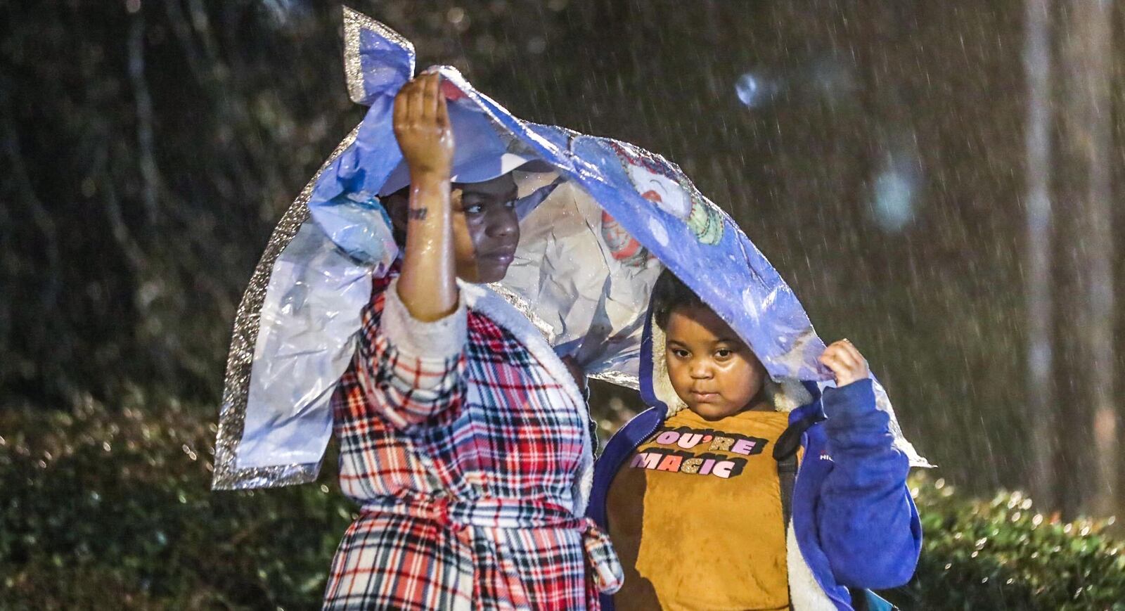 Tyiesha McCane (left) covers 7-year-old Makilha McCane, a first grader at Riverside Primary School, as they wait in the rain for the school bus in Austell.