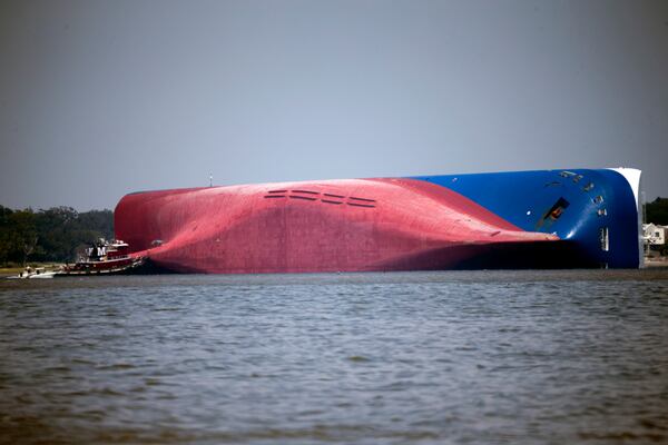 FILE - In this Sept. 9, 2019, file photo, a Moran tugboat nears the stern of the capsizing vessel Golden Ray near St. Simons Sound off the coast of Georgia. The salvage team salvage team is seeking a federal permit to surround the shipwreck with a giant mesh barrier to contain any debris when they cut the ship apart. (AP Photo/Stephen B. Morton, File)