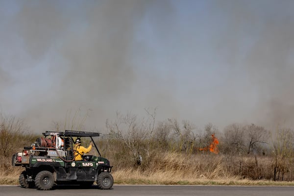 San Antonio Fire Department firefighters head towards a flame at the scene of a large brushfire on Tuesday, March 4, 2025, in Elmendorf, Texas. (Josie Norris/The San Antonio Express-News via AP)