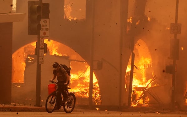 A cyclist pedals past a burning structure on Lake Avenue, Wednesday, Jan. 8, 2025, in the downtown Altadena section of Pasadena, Calif. (AP Photo/Chris Pizzello)