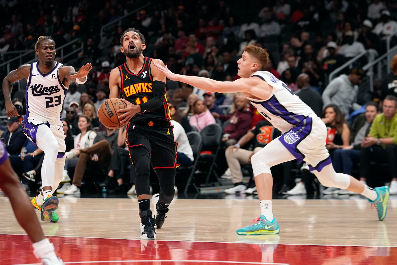 Atlanta Hawks guard Trae Young (11) drives between Sacramento Kings' Keon Ellis (23) and Kevin Huerter (9) during the first half of an NBA basketball game, Friday, Nov. 1, 2024, in Atlanta. (AP Photo/ John Bazemore )