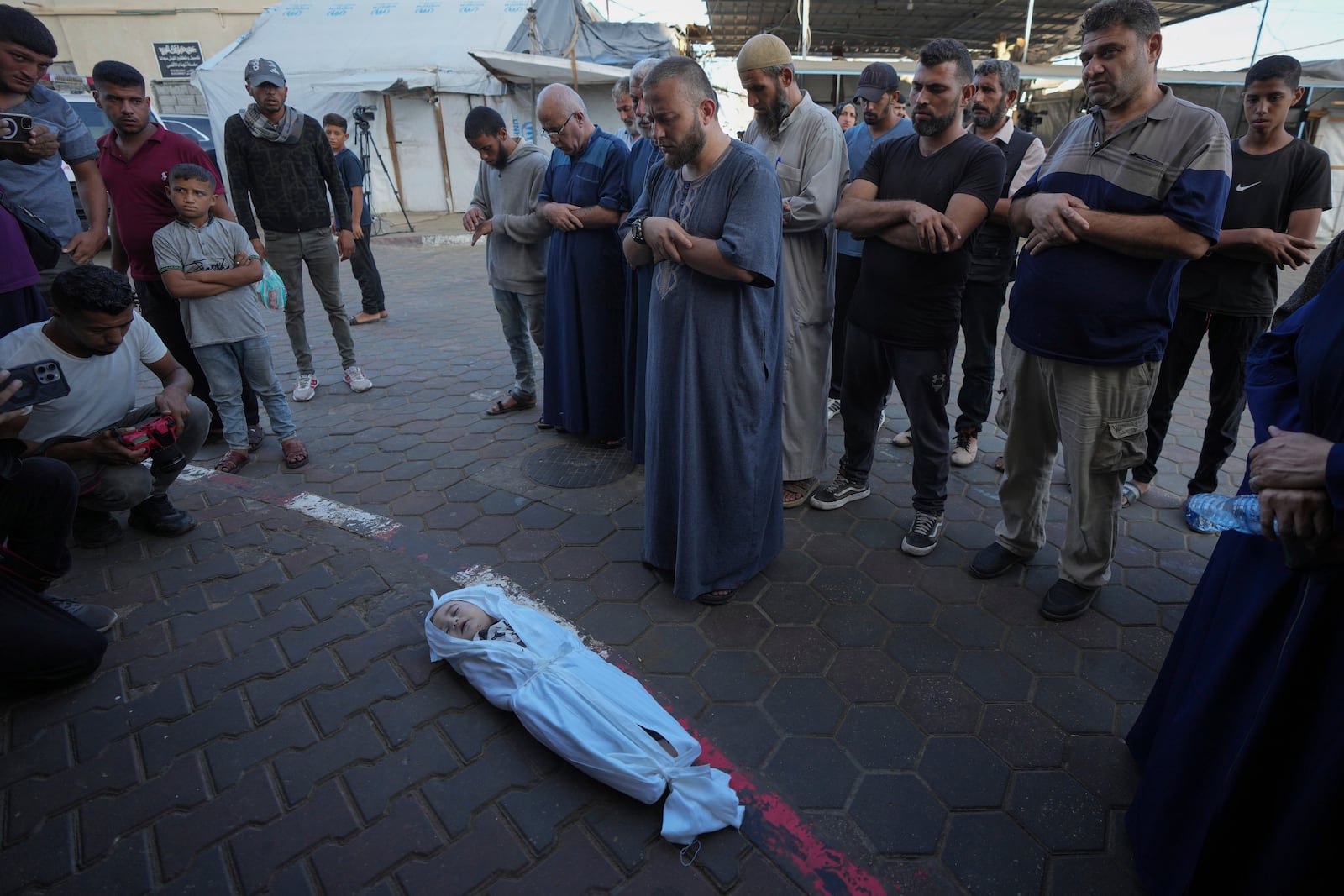 Mourners pray over the body of a Palestinian child, Hosam Al Khaldi, killed in the Israeli bombardment of the Gaza Strip outside the hospital morgue in Deir al-Balah on Wednesday, Oct. 9, 2024. (AP Photo/Abdel Kareem Hana)