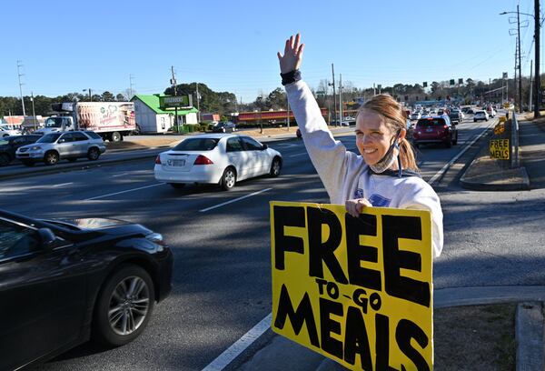 January 29, 2021 Norcross - Janice Osborne, volunteer, holds a sign on Jimmy Carter Blvd to draw attention as Chef Hank Reid and volunteers hand out ready-to eat meals at the parking lot of The Nett Church in Norcross on Friday, January 29, 2021. Hank Reid has been driving a food truck to carry meals where they're needed in Gwinnett County. (Hyosub Shin / Hyosub.Shin@ajc.com)