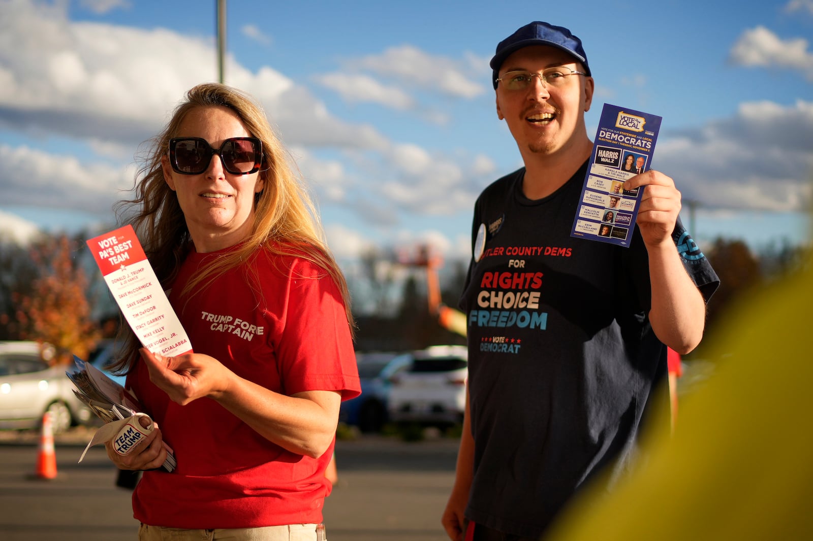 Ingrid Bender, a supporter of Republican presidential nominee former President Donald Trump, left, and Jonathan Foust, a supporter of Democratic presidential nominee Vice President Kamala Harris, offer rosters of who to vote for in their political parties to voters arriving at a polling place in Cranberry, Pa., on Election Day, Tuesday, Nov. 5, 2024. (AP Photo/Robert F. Bukaty)