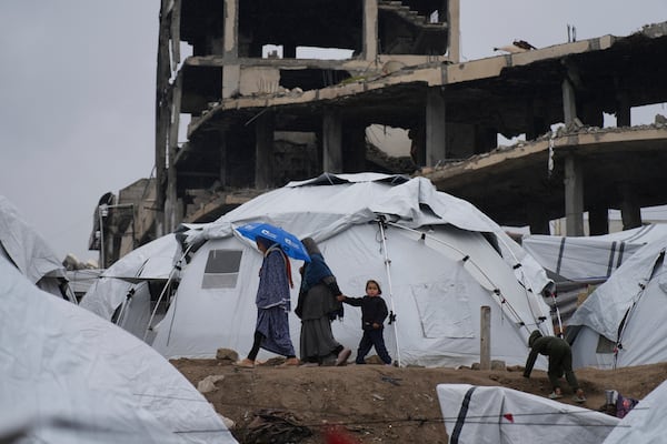 A Palestinian family walk between tents in a sprawling tent camp adjacent to destroyed homes and buildings in Gaza City, Gaza Strip, Saturday, March 1, 2025 during the Muslim holy month of Ramadan. (AP Photo/Abdel Kareem Hana)