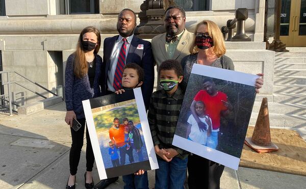 Family members of the late Antonio May and their lawyers stand on the steps of the Fulton County Courthouse following the indictment of six deputies. In the foreground are two of May's three sons holding family photos. Top row from left, Shonna Rickerson, the boys' mother; attorneys Michael Harper and Teddy Reese; and April Myrick, legal guardian of both boys.