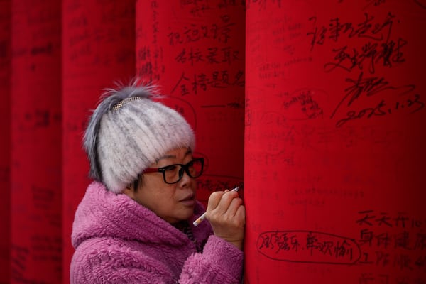 A woman writes wishes on a red cloth roll as people visit a temple fair held at the Dongyue Temple on the first day of the Chinese Lunar New Year in Beijing on Wednesday, Jan. 29, 2025. (AP Photo/Andy Wong)