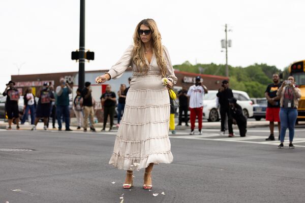 Debbie Wade, wife of recently deceased hip-hop pioneer Rico Wade, sprinkles flower petals at the intersection of Headland and Delowe, a hip-hop landmark in East Point, during her husband’s funeral procession on Friday, April 26, 2024. (Arvin Temkar / AJC)