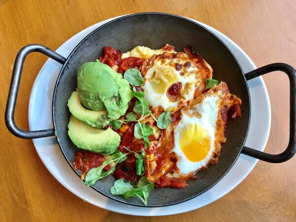 Southern Shakshuka at Tupelo Honey features two baked eggs in a Creole sauce over goat cheese grits. The dish is garnished with fresh avocado slices and lamb’s lettuce. LIGAYA FIGUERAS / LFIGUERAS@AJC.COM