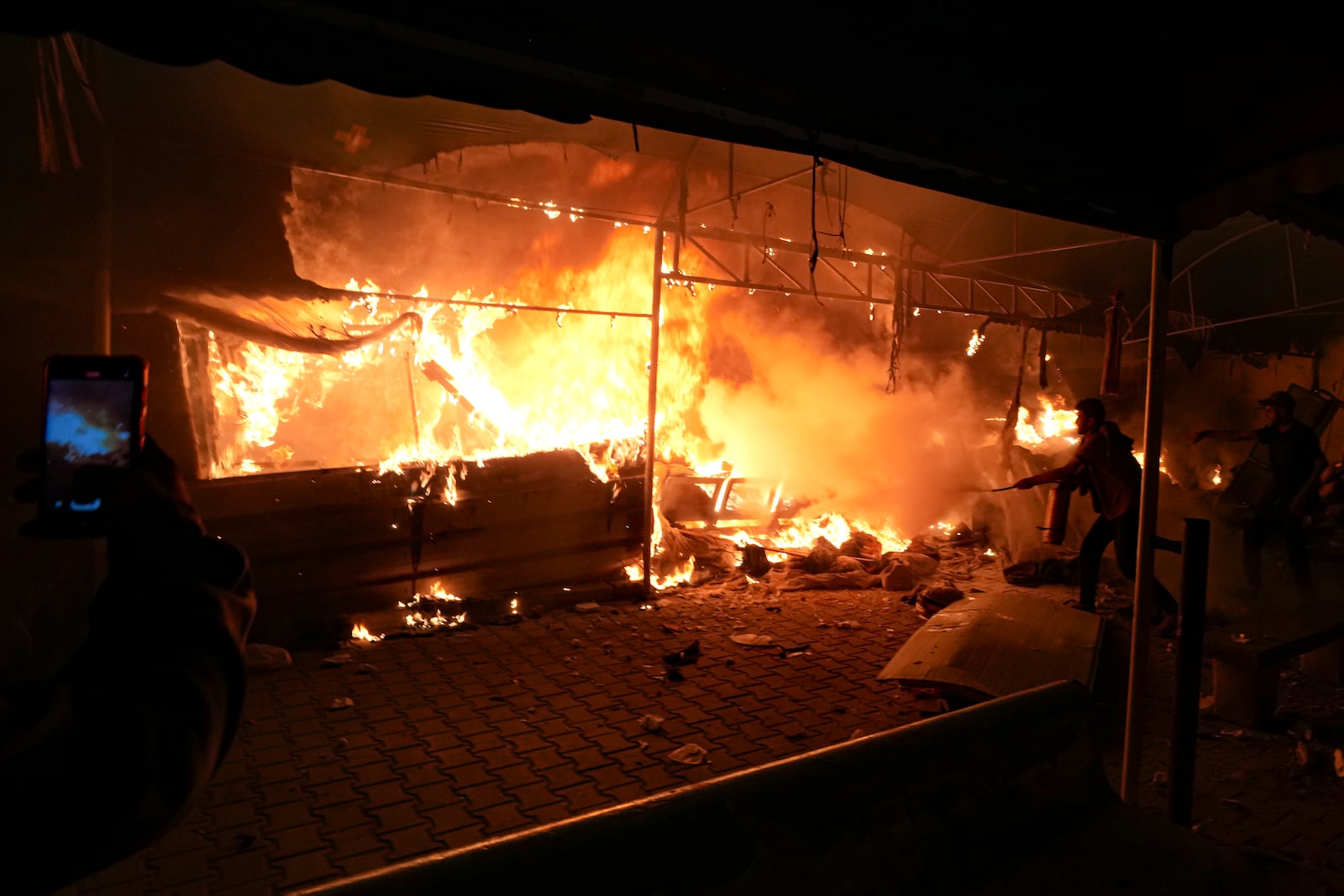 Palestinians tries to extinguish fire caused by an Israeli strike that hit a tent area in the courtyard of Al Aqsa Martyrs hospital in Deir al Balah, Gaza Strip, Monday, Oct. 14, 2024. (AP Photo/Abdel Kareem Hana)