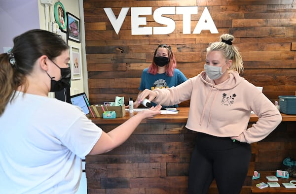 Alixx Hetzel (right) co-owner, offers a gym member Kelsey Cortez (left) a hand sanitizer as she checks in at VESTA Movement Ponce in Atlanta on Wednesday. (Hyosub Shin / Hyosub.Shin@ajc.com)