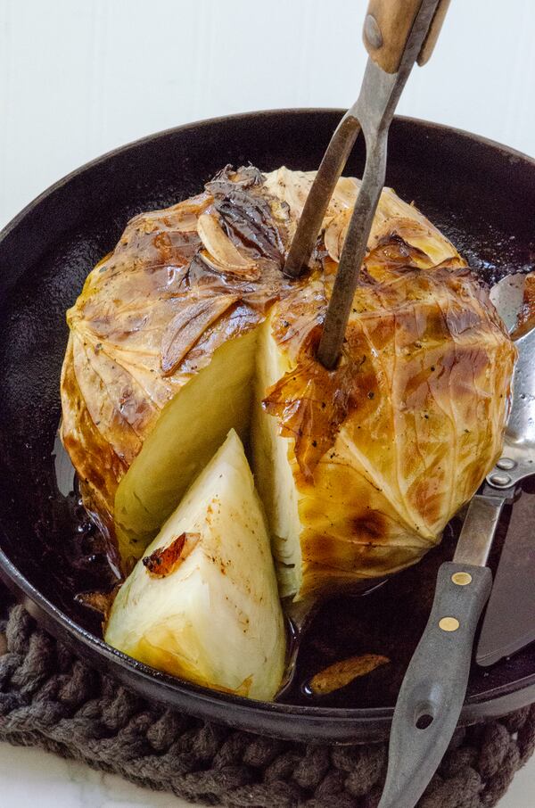 A whole cabbage becomes a stunning dish when drizzled with olive oil, topped with garlic slivers and roasted until golden brown and tender. (Virginia Willis for The Atlanta Journal-Constitution)