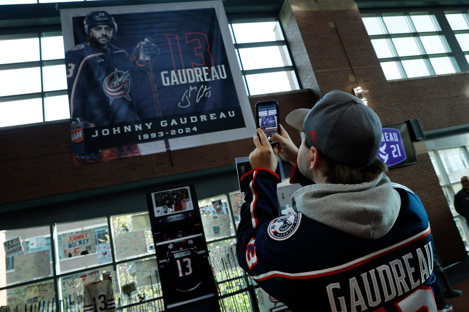 Troy Ward, of Dayton, takes photos of a memorial of Columbus Blue Jackets' Johnny Gaudreau and his brother Matthew before the start of an NHL hockey game against the Florida Panthers. Tuesday, Oct. 15, 2024, in Columbus, Ohio. (AP Photo/Jay LaPrete)