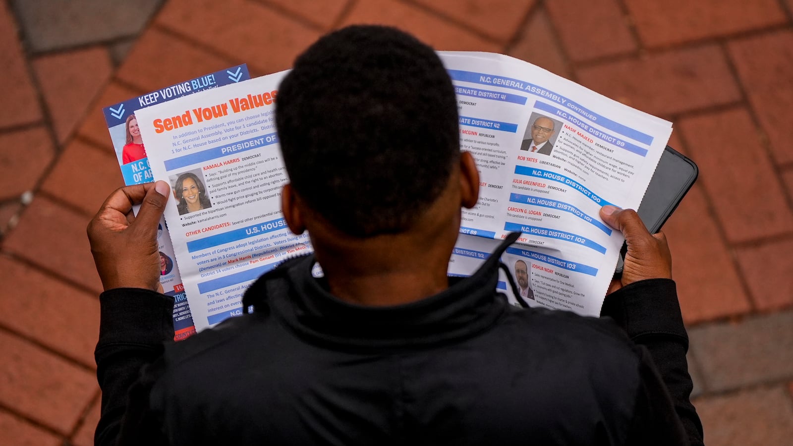 A man reads election materials before voting during the last day of early voting, Saturday, Nov. 2, 2024, in Charlotte, N.C. (AP Photo/Mike Stewart)