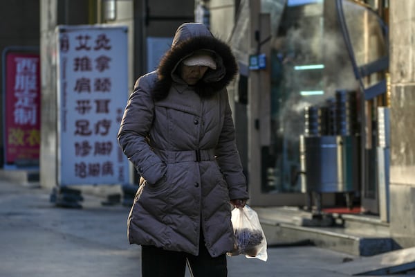 A woman carries a bag of foods as she walks by restaurant and shops in Beijing, Thursday, March 6, 2025. (AP Photo/Andy Wong)