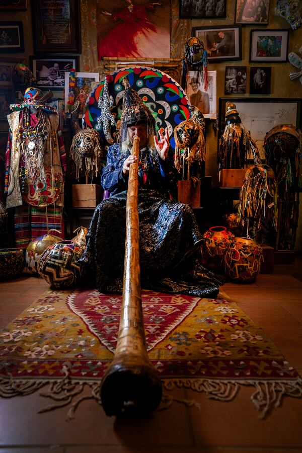 Michael Pierce in his colorful handpainted wearable art blowing a didgeridoo in his home in Farmington.
(Courtesy of Terry Allen)