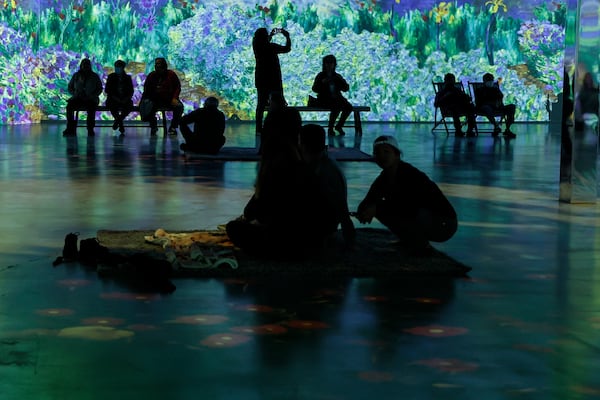 Visitors sit and watch projections on 40 foot walls at “Monet: The Immersive Experience” on Friday, October 28, 2022. (Natrice Miller/natrice.miller@ajc.com)  