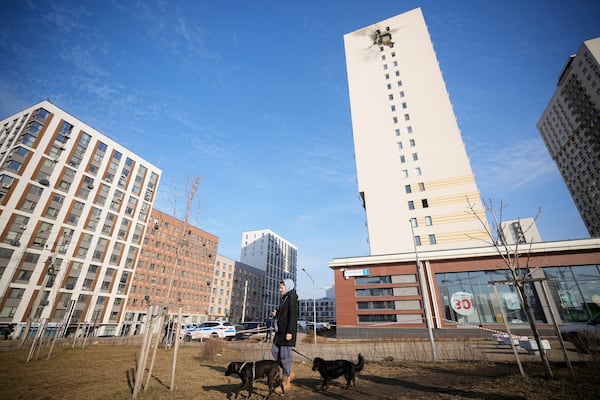 A local citizen walks with two dogs near an apartment building, right, where a downed Ukrainian drone fell at an area in Sapronovo village outside Moscow, Russia, on Tuesday, March 11, 2025. (AP Photo)