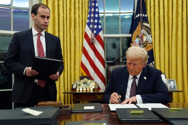 President Donald Trump signs an executive order to create the Department of Government Efficiency (DOGE) in the Oval Office of the White House on Jan. 20 in Washington, as White House staff secretary Will Scharf watches. (AP Photo/Evan Vucci)