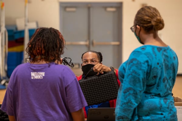 Kendell Higgs (center), technician for Clayton County Public Schools Extended Learning Beyond the Classroom, hands a student a laptop during distribution at Edmonds Elementary School in Forest Park on Oct. 14, 2020.  (Alyssa Pointer / Alyssa.Pointer@ajc.com)