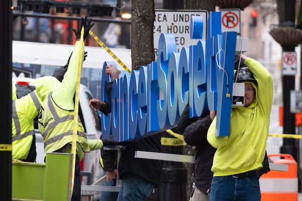 Workers install a sign on the American Cancer Society’s new headquarters along Peachtree Street in downtown Atlanta on Thursday, Dec. 26, 2024. Ben Gray for the AJC