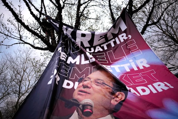 A man attaches a large banner of Istanbul's Mayor Ekrem Imamoglu in a tree in Istanbul, Turkey, Thursday, March 20, 2025, during a protest against the arrest of Imamoglu. (AP Photo/Emrah Gurel)