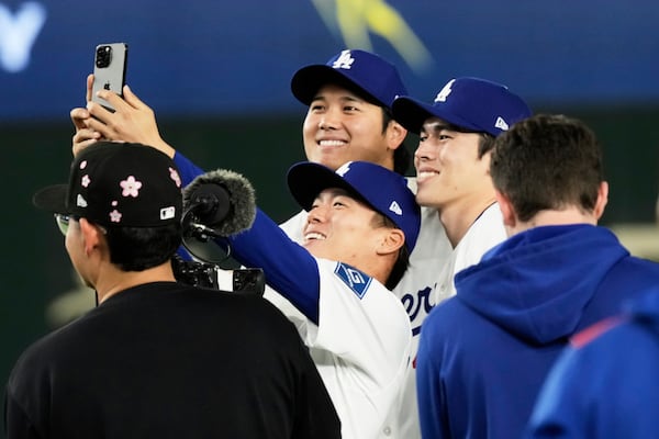 Los Angeles Dodgers starting pitcher Yoshinobu Yamamoto, center, takes a photo with Shohei Ohtani, left rear, and Roki Sasaki, right rear, following the team's MLB Tokyo Series baseball game against the Chicago Cubs in Tokyo, Japan, Wednesday, March 19, 2025. (AP Photo/Hiro Komae)