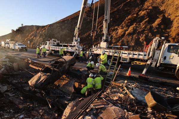 Workers pull a burnt car out of the wreckage of a home destroyed by the Palisades Fire, Tuesday, Jan. 14, 2025, in Malibu, Calif. (AP Photo/Ethan Swope)