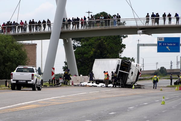 Pedestrians standing on a bridge watch emergency officers investigate a bus that overturned on a highway in Johannesburg, South Africa, Tuesday, March 11, 2025, killing multiple people and injuring some. (AP Photo/Alfonso Nqunjana)