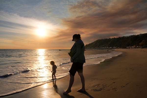 Malibu residents Florence Johnson and her son Brian enjoy the beach before sunset as a plume of smoke from the Franklin Fire rises over the ocean Tuesday, Dec. 10, 2024, in Malibu, Calif. (AP Photo/Damian Dovarganes)