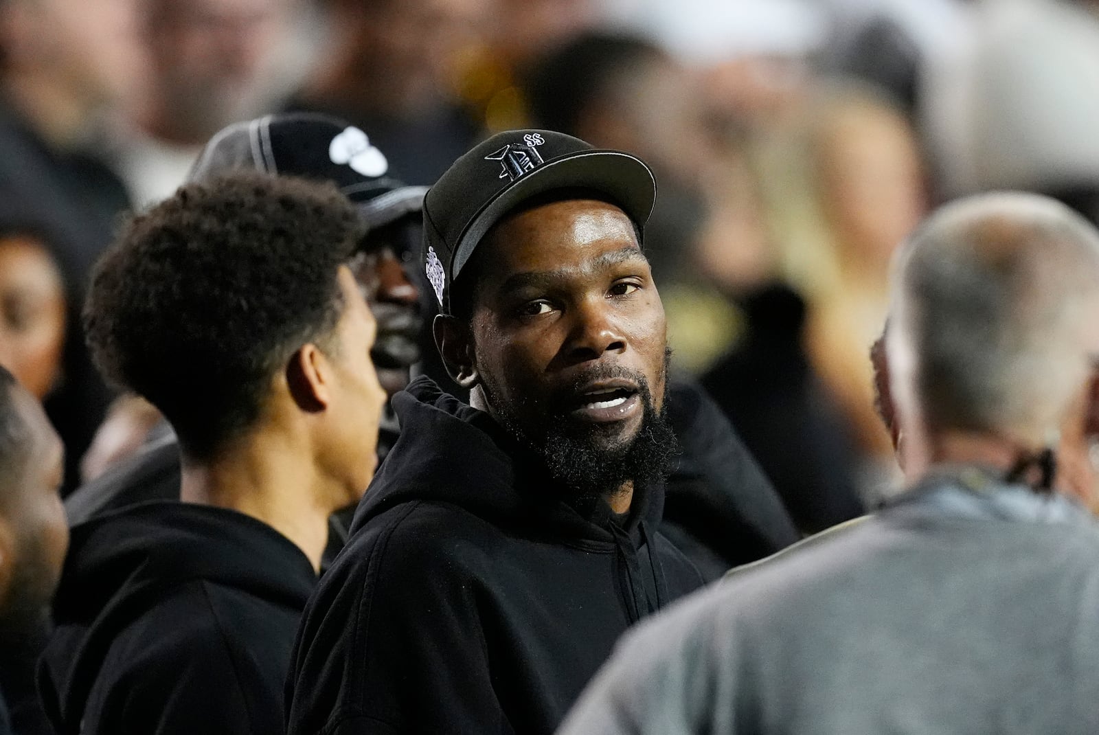 Phoenix Suns forward Kevin Durant, center, talks with teammates as they watch Colorado host Kansas State in the first half of an NCAA college football game Saturday, Oct. 12, 2024, in Boulder, Colo. (AP Photo/David Zalubowski)