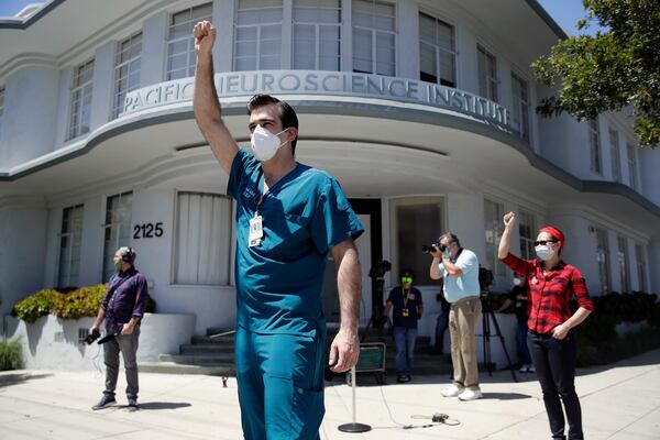 Nurses Michael Gulick, center, and Angela Gatdula, far right, hold their arms up in protest outside of Providence Saint John's Health Center  in Santa Monica, Calif. The hospital suspended 10 nurses, including Gulick, from their jobs last week after they refused to care for COVID-19 patients without being provided protective N95 face masks. Gatdula contracted COVID-19 while working in the hospital and has recovered. 