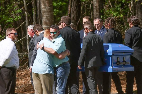 Two people hug as pall bearers carry the casket of a Hawk family member on Thursday, April 14, 2022, in Newnan, Ga.  The Coweta family was killed during a gun shop robbery.   Branden Camp/For the Atlanta Journal-Constitution