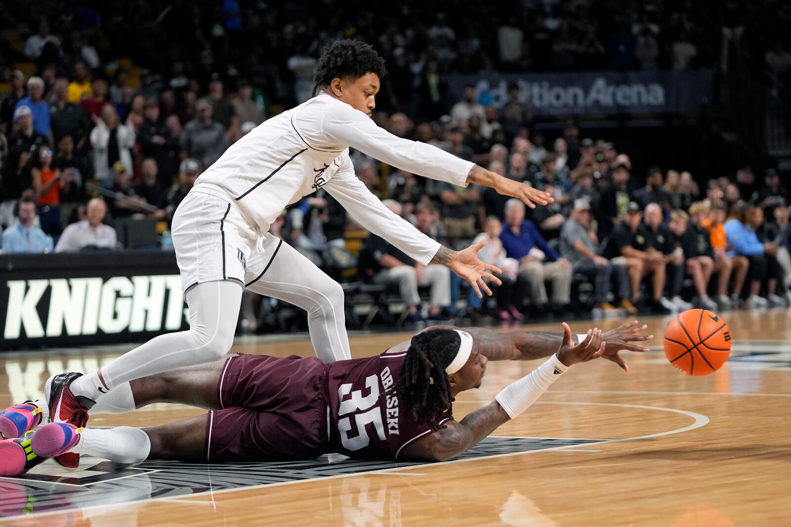 Texas A&M guard Manny Obaseki (35) passes the ball as he falls in front of Central Florida guard Dior Johnson, top, during the first half of an NCAA college basketball game, Monday, Nov. 4, 2024, in Orlando, Fla. (AP Photo/John Raoux)