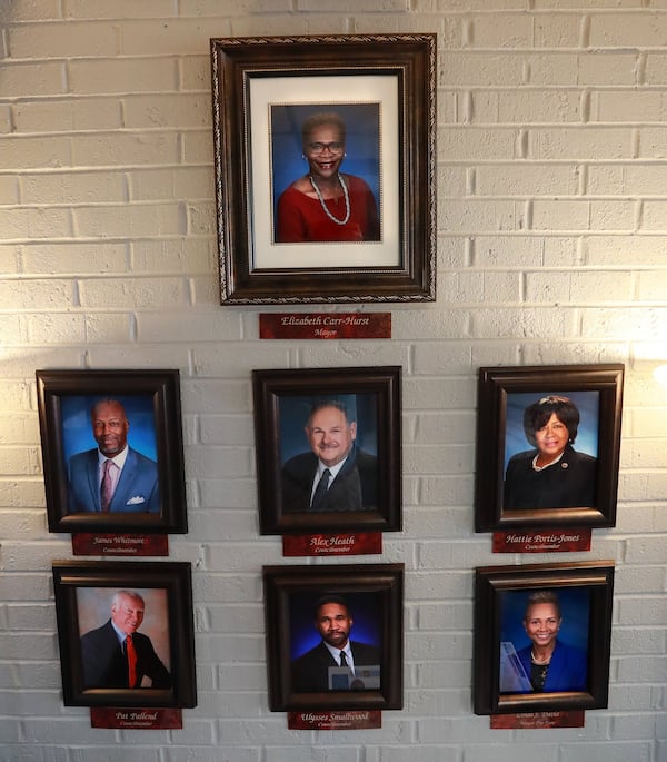 A portrait of Mayor Elizabeth Carr-Hurst hangs on the wall above Councilmembers James Whitmore, Alex Heath, Hattie Portis-Jones, Pat Pallend, Ulysses Smallwood, and Linda Davis at City Hall on Monday, August 12, 2019, in Fairburn. CURTIS COMPTON/CCOMPTON@AJC.COM