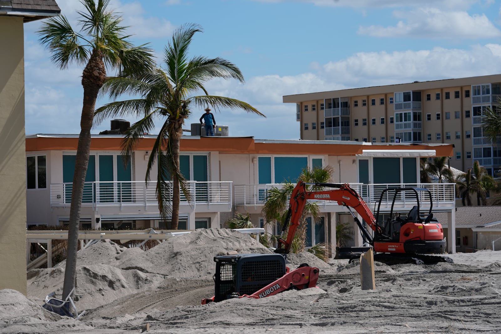 Scott Bennett, a contractor who specializes in storm recovery, drives a skid steer, bottom, as he removes sand around 5 feet deep from the patio of a beachfront condominium in Venice, Fla., following the passage of Hurricane Milton, Saturday, Oct. 12, 2024. Bennett said he had just finished digging out the same condominium complex after Hurricane Helene, when Milton buried it in an even deeper layer of sand. Before Helene hit, the Venice native said, he'd "never seen sand like this. Wind rain, water, but never sand." (AP Photo/Rebecca Blackwell)