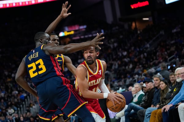 Atlanta Hawks guard Trae Young, right, looks for an open teammate while defended by Golden State Warriors forwards Draymond Green, left, and Andrew Wiggins during the first half of an NBA basketball game Wednesday, Nov. 20, 2024, in San Francisco. (AP Photo/Godofredo A. Vásquez)