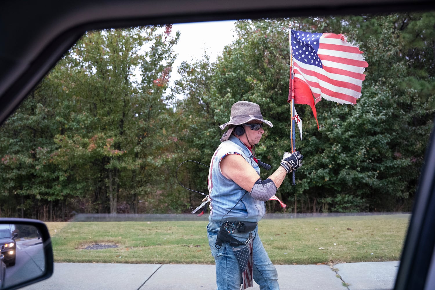 A man carries a tattered American flag along the side of the road on election day in Norcross, Georgia, Tuesday, Nov. 5, 2024. (Olivia Bowdoin for the AJC). 