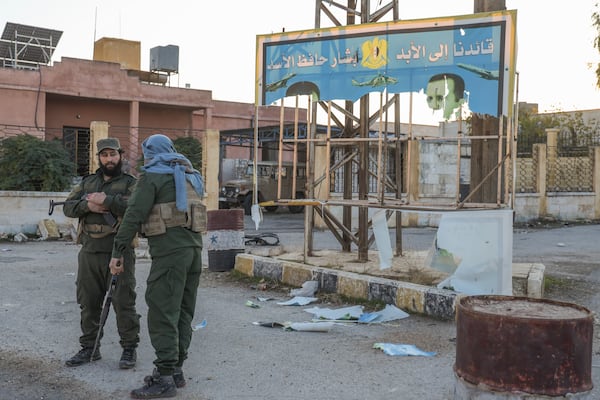 Syrian opposition soldiers stand next to a government sign in Anjara, western outskirts of Aleppo, Syria, Thursday Nov. 29, 2024. Syrian armed groups launched a large-scale attack on areas controlled by government forces and seized territory in northwestern Syria, opposition groups said Thursday.(AP Photo/Omar Albam)