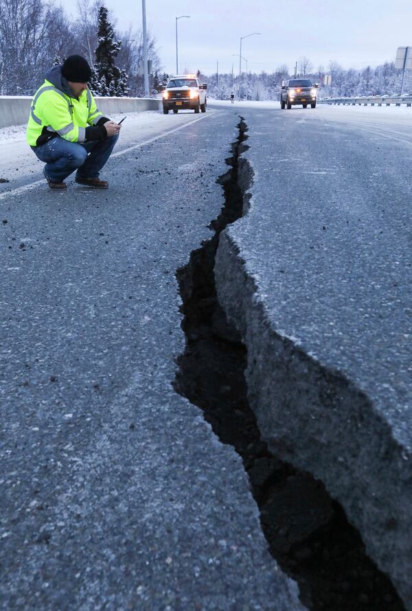 Marty Thurman with Granite construction inspects a crack in the road at the International Airport Road offramp on southbound Minnesota Blvd., in Anchorage, Alaska, Friday, Nov. 30, 2018. A state official says Ted Stevens Anchorage International Airport is open and operating at reduced capacity with delayed flights following back-to-back earthquakes.