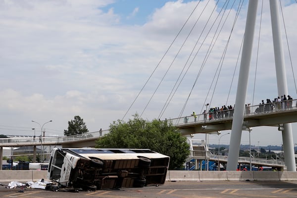 Pedestrians standing on a bridge look at a bus that overturned on a highway in Johannesburg, South Africa, Tuesday, March 11, 2025, killing multiple people and injuring some. (AP Photo/Alfonso Nqunjana)